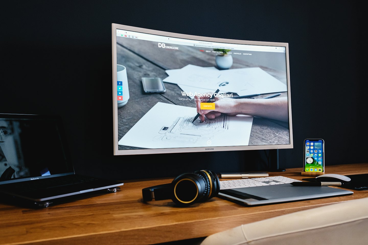 Designer's desk with curved monitor, laptop, and graphics tablet.